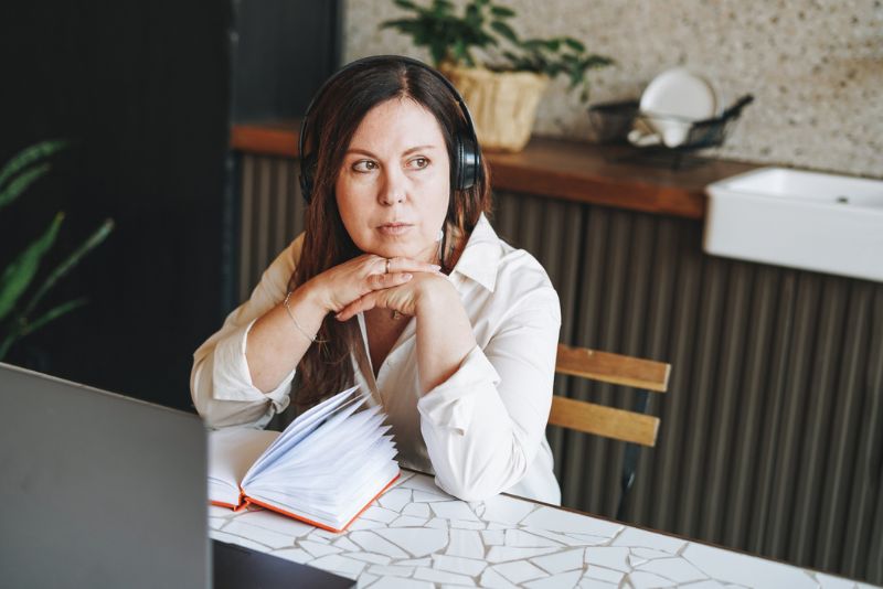 Vrouw zit aan bureau en kijkt peinzend voor zich uit